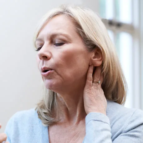 Mature woman experiencing hot flush from menopause and using a hand-held fan for relief.