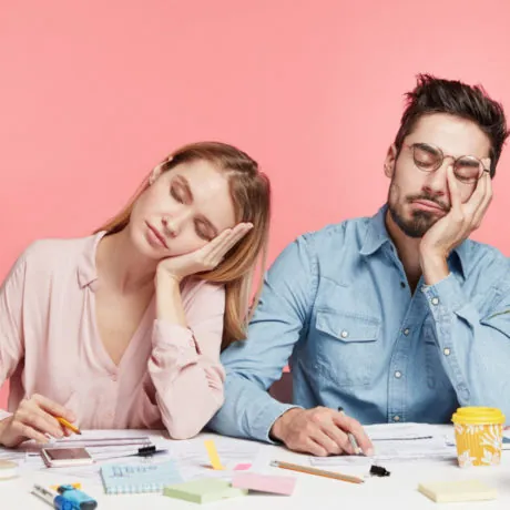 Portrait tired crew of office workers sit at table, fall asleep after working long hours on preparing startup project, feel tiredness, isolated over pink background. People and overworking concept