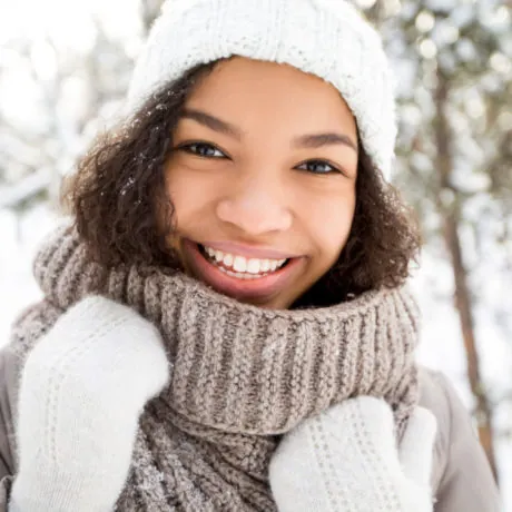 Portrait of teenage African American girl wearing warm clothing walking, looking at camera and laughing in winter