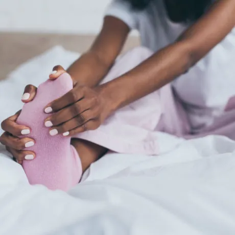 cropped view of african american woman suffering from foot pain in bedroom