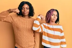 Beautiful african american mother and daughter wearing wool winter sweater strong person showing arm muscle, confident and proud of power