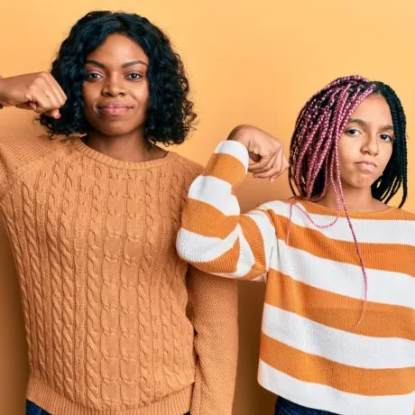 Beautiful african american mother and daughter wearing wool winter sweater strong person showing arm muscle, confident and proud of power