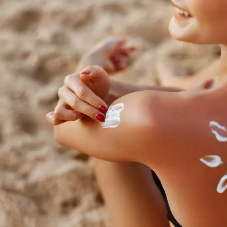 Young woman with sun shape on the shoulder holding sun cream bottle on the beach