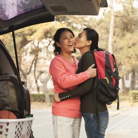Mother and daughter embracing behind car on college campus