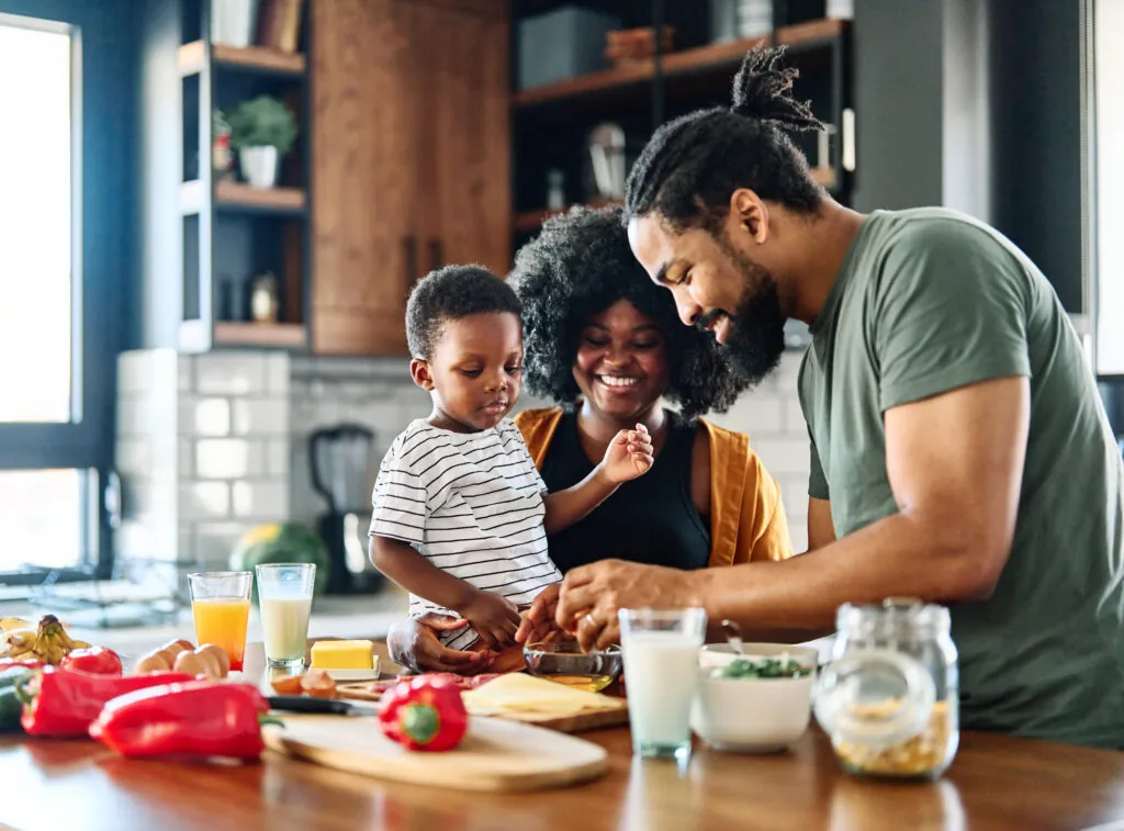 Portrait of mother, father and son preparing and eating breakfast in the kitchen at home