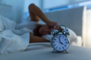 Woman in bed, frustrated because she can't sleep and staring at her alarm clock.