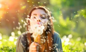 Beautiful young woman lying down on the field in green grass, blowing dandelions
