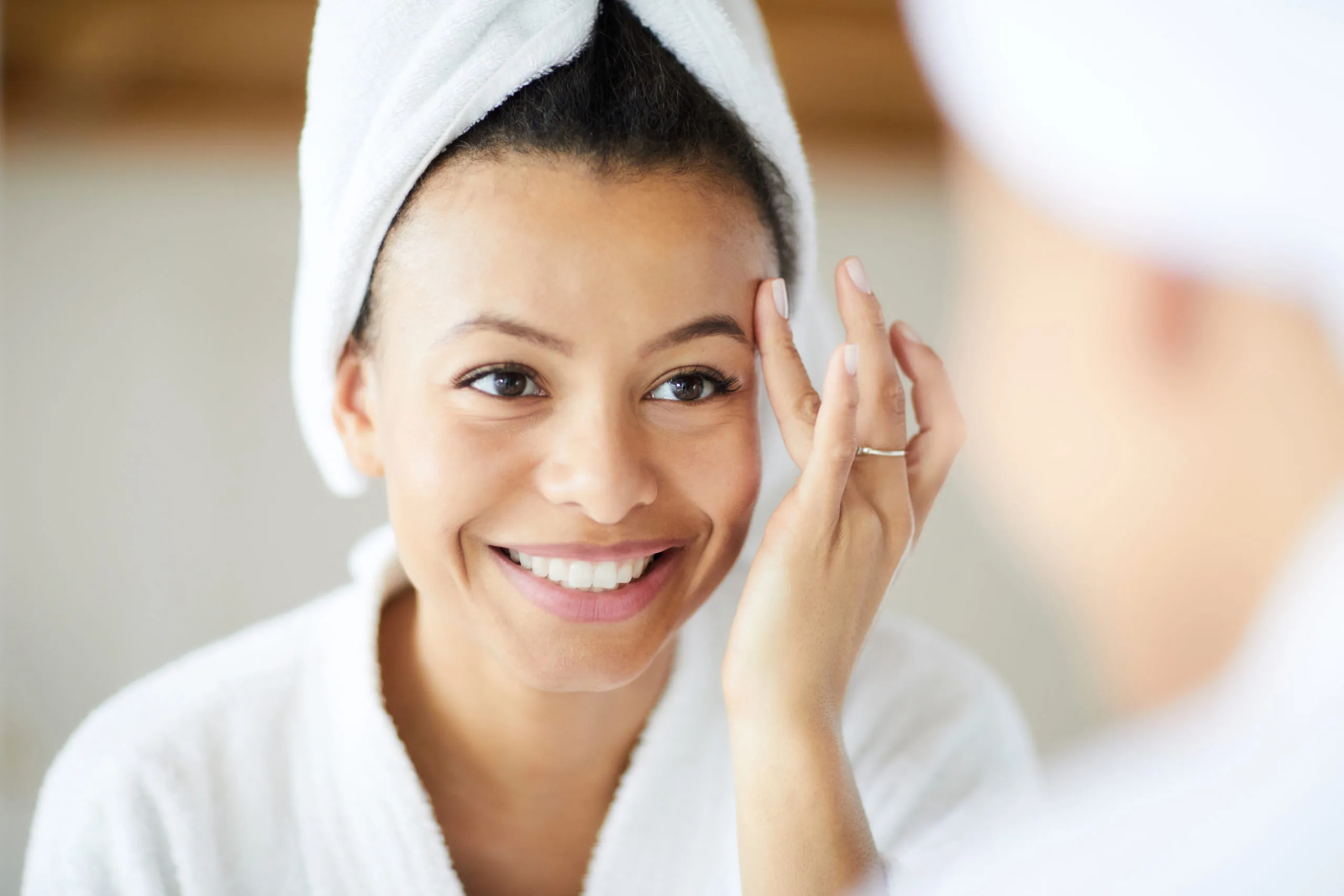 Head and shoulders portrait of smiling Mixed-Race woman applying face cream during morning routine