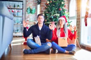 Young couple wearing santa claus hat sitting on the floor around christmas tree at home relax and smiling with eyes closed doing meditation gesture with fingers.