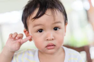 Little asian toddler baby boy has earache when insects inside outdoor baby infant boy hands touching in ear and pain.deaf kid.Flu and sick.Clean up earwax.Accident in kid with ear.Condition and clean.