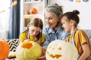 Three generations carving pumpkins for halloween, sharing laughter and creativity. Smiling girls, guided by loving grandmother, creating cherished family memories. Celebration concept