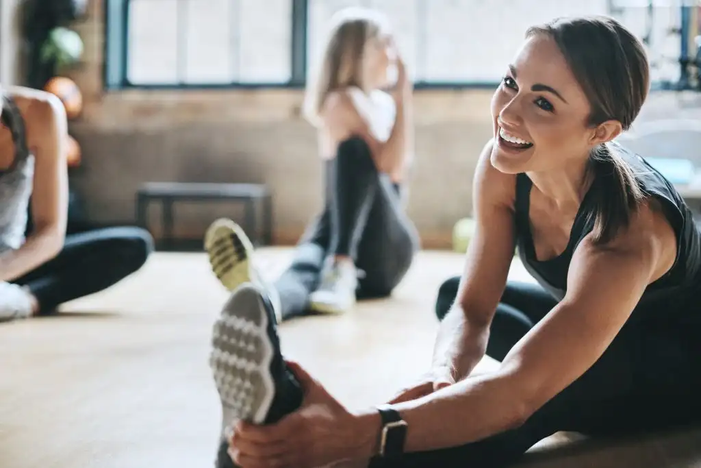 Fitness, gym and women stretching, exercise and workout goal for wellness, balance and stress relief. Female people, girls and athletes on the floor, stretch legs and smile with training and health