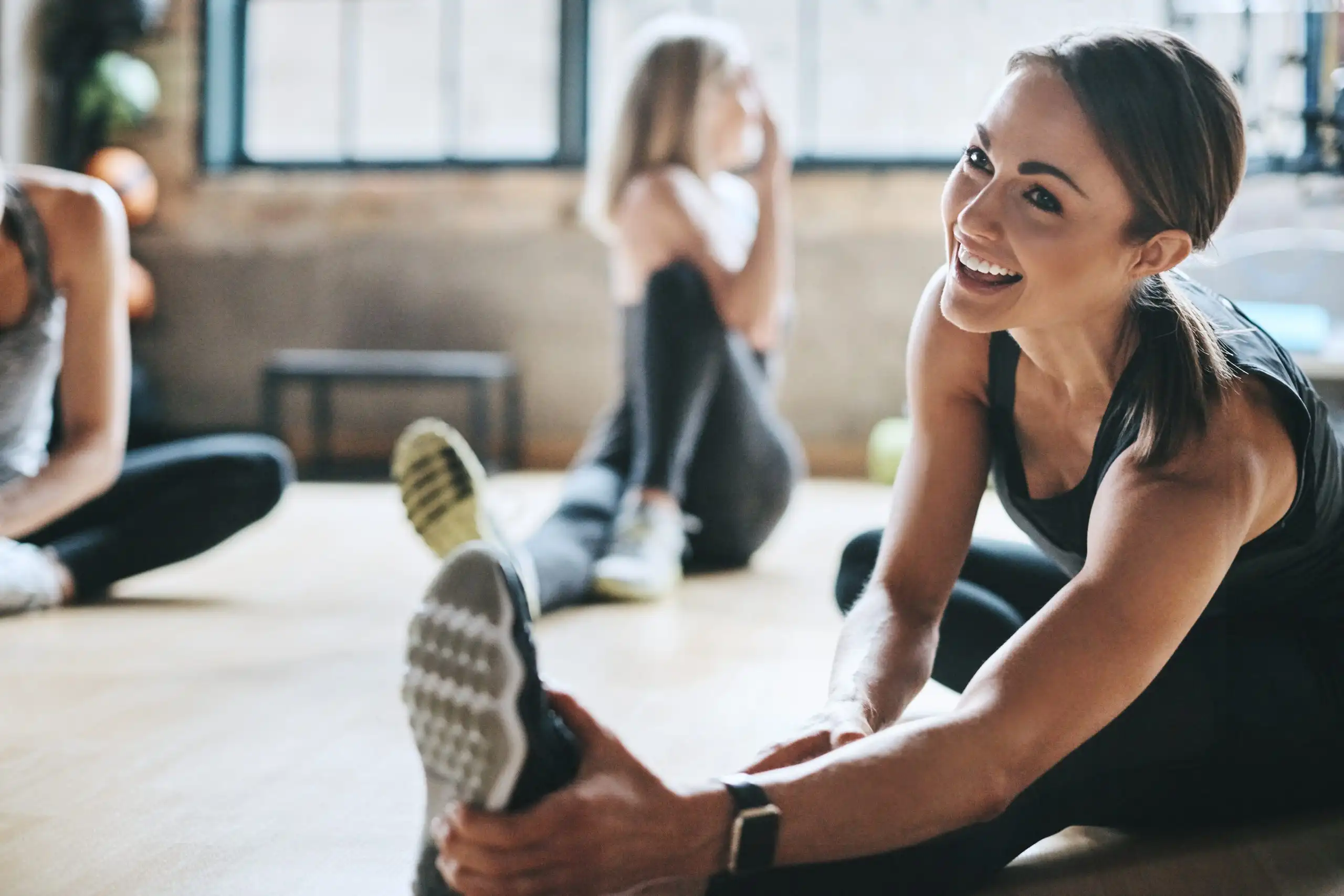 Fitness, gym and women stretching, exercise and workout goal for wellness, balance and stress relief. Female people, girls and athletes on the floor, stretch legs and smile with training and health