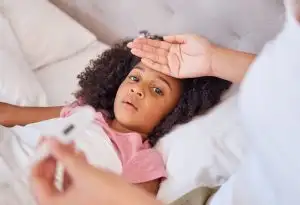 mother with sick daughter in bed, reading temperature with thermometer for fever in bedroom. Health, children and hand of worried mom caring for unhealthy child with corona symptoms