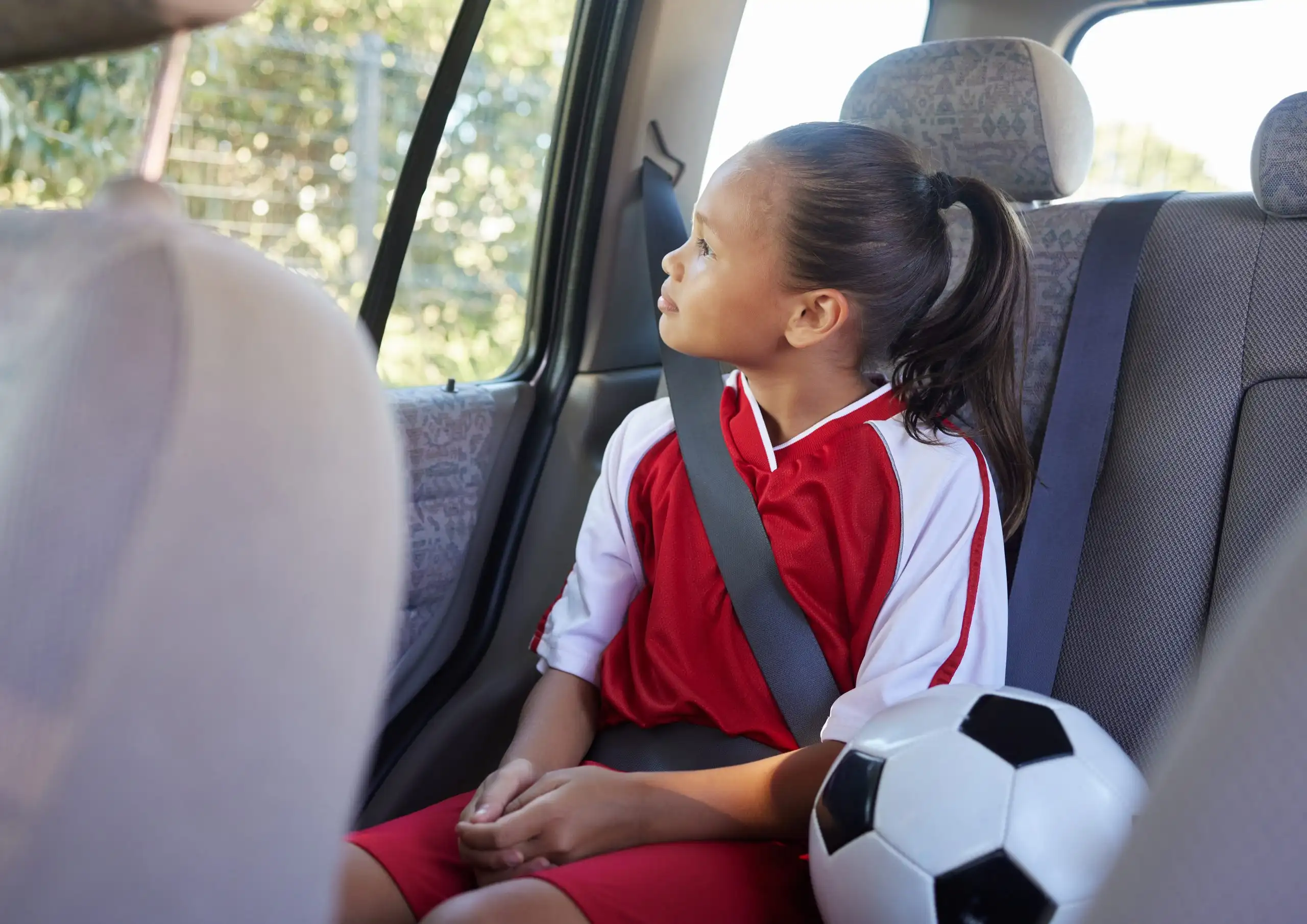 Child in car interior, travel transport to football and soccer athlete sitting in motor vehicle. Young sports athlete in Brazil fitness training, journey to game in back seat and kid safety seat belt